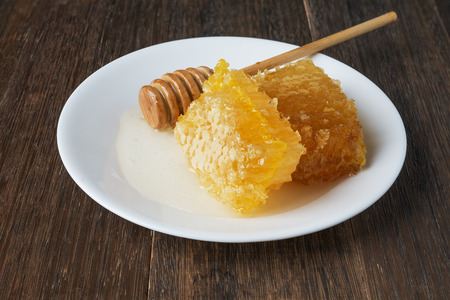 Golden honeycomb and honey stick on a white plate  on vintage wooden tableの写真素材