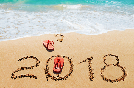 Red flip flops and digits 2018 on the beach sand.Concept of summer vacations, new year  and   Christmasの写真素材
