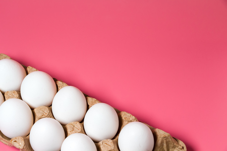 Fresh chicken eggs background. White eggs in craft carton pack on pink background with copy space. Perspective. Natural healthy food and organic farming concept. Close up.の写真素材