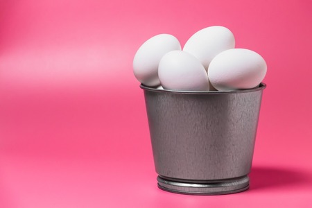 White eggs in metal bucket on pink background. Easter minimal concept. Front view. Close up. Copy...