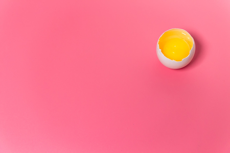 Fresh farm chicken egg, food background. Cracked egg with white and yolk over pink. Spring easter theme. Close up. Copy space.の写真素材
