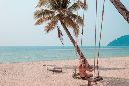 girl swinging on a swing tied to a palm tree by the seaの写真素材