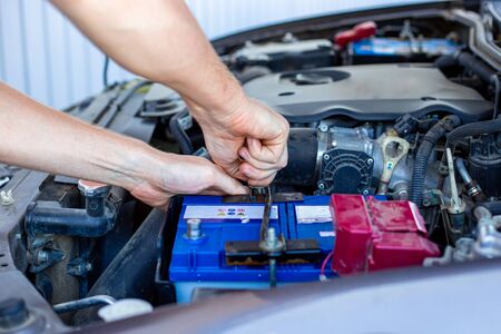 repair and installation of the battery under the hood of a car, a man works in a car serviceの写真素材