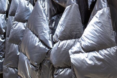warm gray silver jackets hang on hangers in a store, fabric backgroundの写真素材