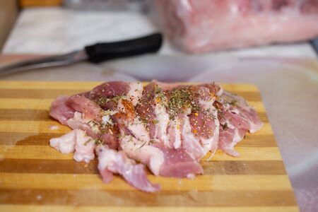 raw meat pork on a cutting wooden board, sprinkled with seasonings, next to a knife, selective focus