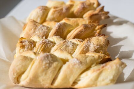 fresh pastries from puff pastry in the form of braided braids lie on parchment paper, sweet puffs...