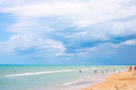 Anapa, Russia - 08/06/2019: summer beach with tourists walking and swimming in the azure sea under a blue sky, vacation on the sea coast, the end of quarantine and self-isolationのeditorial素材