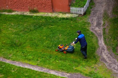worker mows grass with a mower in the backyard of a house, summer day in the cityの写真素材