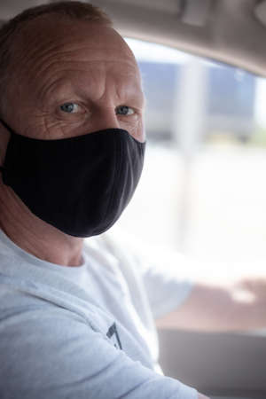 European adult man in a black protective mask is sitting in a car interior. The epidemic and...