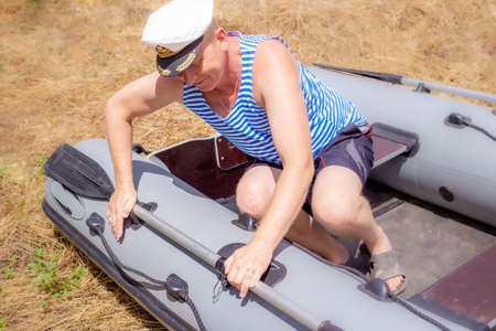 a man in a marine cap sits in a rubber boat standing on the grass, takes the oar. A retired sailor...