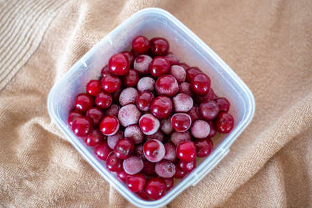 frozen cherries with a bloom of frost on the fruits. Container with red berries. Ingredient for...