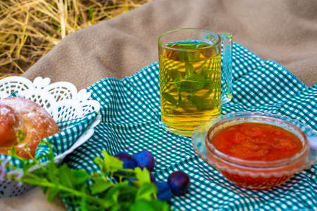 Picnic in nature in autumn. Green tea with mint in a glass cup, a bowl with berry preserves and...