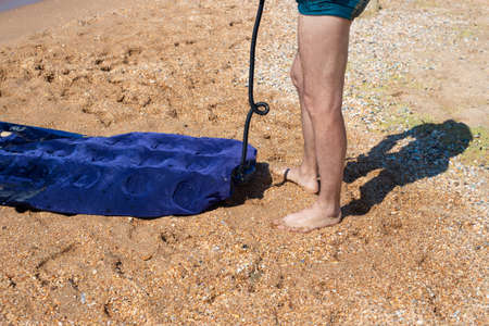 a man in swimming trunks pumps up a rubber mattress on the sand, on the seashore. Swimming on...