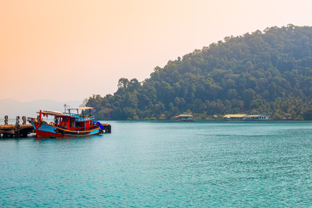 Koh Chang. Thailand-01.18.2020: Thai bright boat at the pier in the sea against the backdrop of green mountains, view from the water. Travel and tourism in Asiaのeditorial素材
