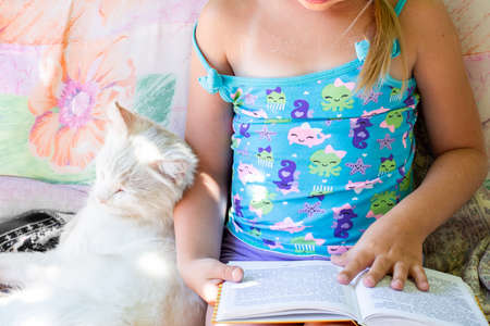 a girl is sitting and reading a book, a white cat is sleeping next to her. Rural life in the village...
