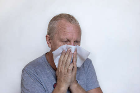 An elderly European man blows his nose, sneezes and coughs into a napkin. Coronavirus infection.の写真素材