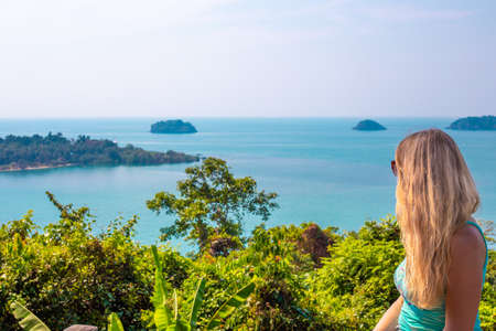 girl with blond hair stands surrounded by greenery on a tropical island and looks at the seaの写真素材