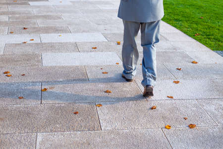 a man in a gray suit walks on paving stones with fallen dry leaves, waist-deep view.の写真素材