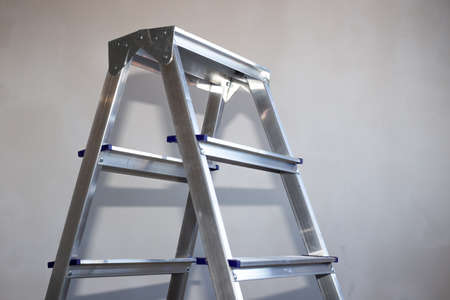 an iron step-ladder stands in a room with gray plastered walls, a copy of the space.