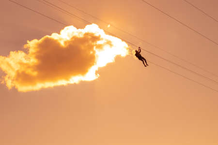 man on a zipline rides high in the sky at sunset. Extreme entertainment.