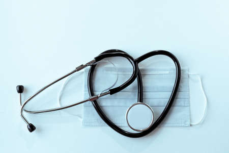 phonendoscope in the shape of a heart and a medical mask on a light background, blue tinted....