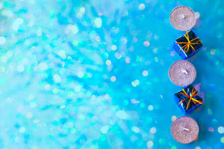 candles and gift boxes on blue background with multicolored bokeh, Christmas minimalistic festive background, flat layout.の写真素材