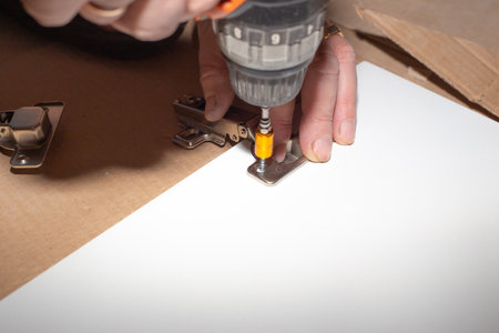 assembling wooden furniture, screwing a metal hinge into the cabinet door of a kitchen set....