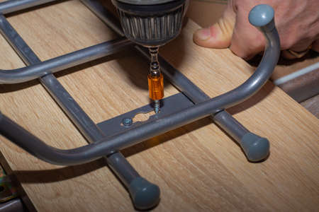 The man works with a screwdriver. Screwing an iron hanger to a wooden surface. Home renovation.