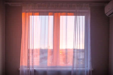 The rays of the morning sun fall through the white tulle on the window in the apartment. Sunrise, new day, atmospheric mood.の写真素材