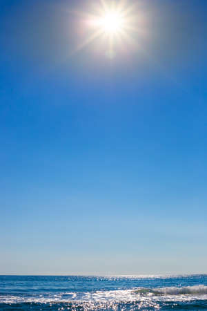 Vertical seascape. Blue sky with bright sun and blue sparkling sea on the horizon. Travel and tourism. Place for your text.の写真素材