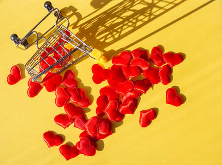 the iron handcart overturned and scattered red hearts on a yellow background. Love, relationship concept.の写真素材