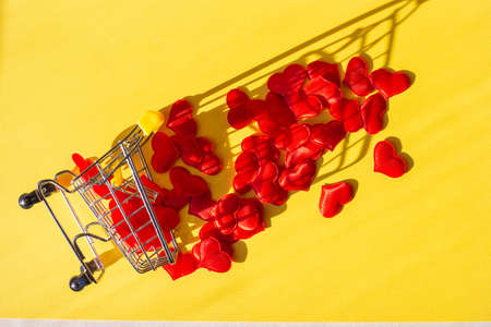 shopping trolley overturned, and red hearts fell out of it, a yellow background. Buy love concept,...
