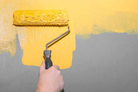A woman paints a gray wall with a roller yellow.
