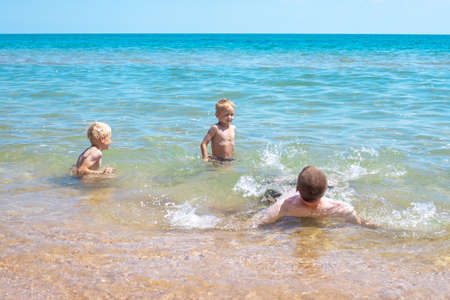 Family dad and two blond sons swim in the sea and laugh. Happy family vacation at the sea.の写真素材