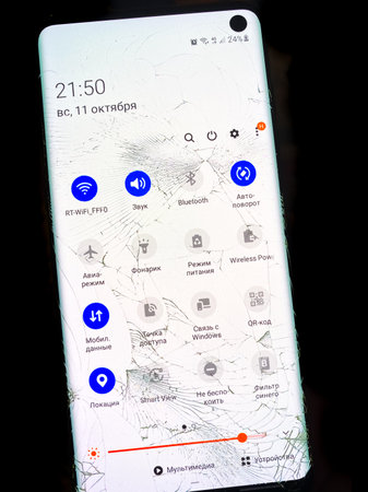 Krasnodar, Russia-11.10.2020: Cracks on the broken glass of a Samsung phone with the screen on on a black background. Glass protection against falling.のeditorial素材