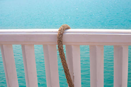 A thick rope hangs on a white wooden pier against the backdrop of sea water.の写真素材