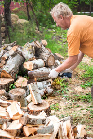 A man chops wood with a large ax in the yard of his house. Procurement of fuel for the winter for heating housing. Selective focus.の写真素材