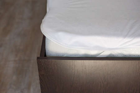 Wooden bed with a high mattress and a covered white mattress cover.の写真素材