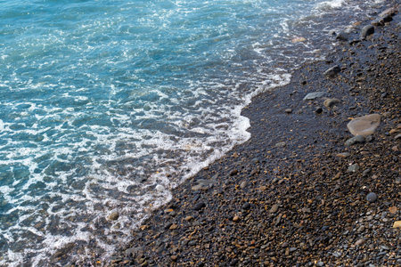 Surf with a pebble beach. Summer vacation at the sea. Natural background with an oncoming wave.