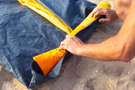 A man is folding a tourist tent. Summer vacation in nature, on the seashore.