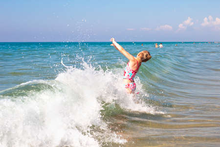 A little girl bathes in the waves of the sea. Fun and fun during the summer holidays.の写真素材