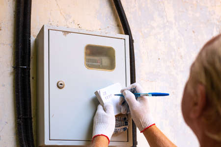 Transfer of readings of an electric meter. A man writes down the numbers of kilowatts.