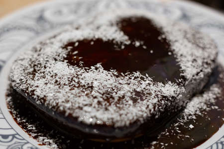 Homemade cake with heart-shaped chocolate icing pattern and coconut chips. Delicious sweet pastries.