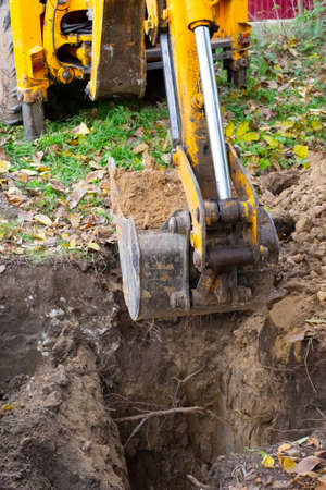 The excavator digs a hole. Yellow arrow with a bucket shovels out the earth, preparing a trench for a sewer well.の写真素材