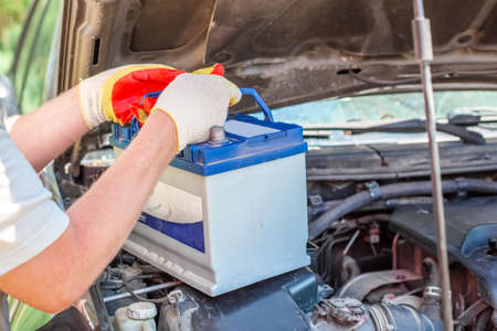 Maintenance of the machine. A male car mechanic takes out a battery from under the hood of a auto to repair, charge or replace it.の写真素材