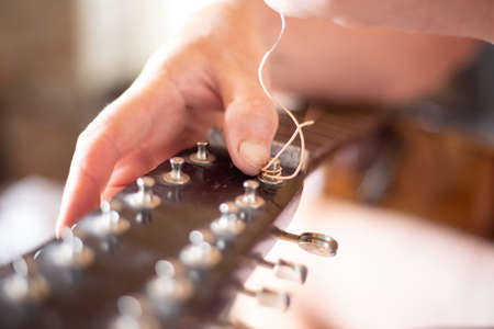 Repair of an old guitar. The man pulls the strings on the fretboard. Selective focus.の写真素材