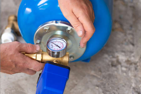 Blue metal tank of a pumping station with a pressure gauge. Installation of a water supply system in...
