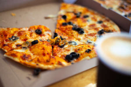 Fresh pizza cut into pieces in a box on the table, blurred focus.