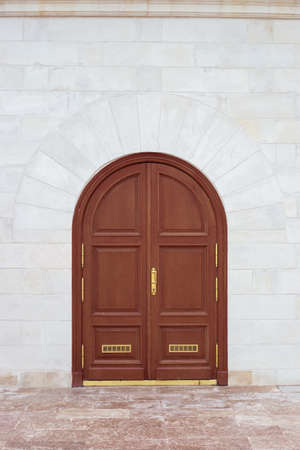 Closed wooden door with an arch in a stone white wall. Design and architecture.
