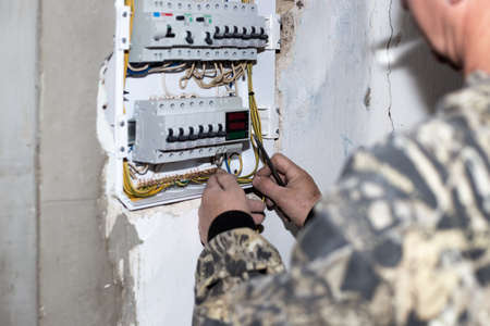 An electrician installs an electrical panel with toggle switches to supply electricity to the house.